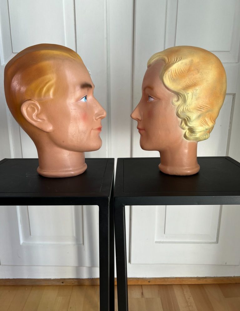 Atomic-Era Ceramic Mannequin Heads – Vintage Display Pair, 1950s–60s Pair of vintage ceramic mannequin heads with stylized features and retro hair, mounted on black stands, c. 1950s–60s